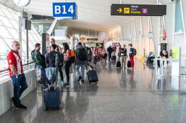Bilbao, İspanya, 4 Nisan 2024: Kırmızı ve beyaz tişörtlü yolcular, futbol karşılaşması görüntülerinden önce B14 kapısının yanında bavullarıyla beklemektedirler.