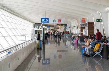 Bilbao, İspanya, 4 Nisan 2024: Yolcular, Bilbao Havalimanı 'nda oturma, cam duvar ve fast food restoranları editoryal imajı bulunan B14 ve B15 biniş kapılarının yanında bekliyorlar