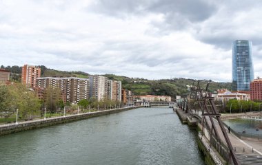 Bilbao, İspanya, 4 Nisan 2024: İberdrola Kulesi ve nehir kenarındaki meskun binalar ve Bilbao 'daki yeşil tepeler, editoryal görüntü