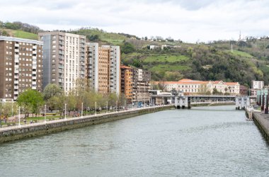 Bilbao, İspanya, 4 Nisan 2024: Nervion Nehri boyunca yeşil tepeler ve Bilbao şehir merkezindeki Puente de Deusto köprüsü boyunca gezinti alanı