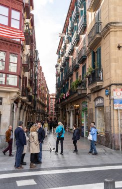 Bilbao, İspanya, 4 Nisan 2024: Bilbao 'da balkonları, bayrakları, dükkanları ve kavşağında yürüyen veya ayakta duran insanlarla dolu dar yaya sokağı, editoryal görüntü