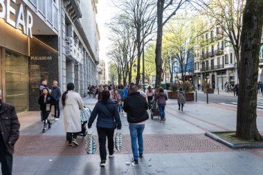 Bilbao, İspanya, 4 Nisan 2024: Alışverişçiler Bilbao 'nun merkezindeki Gran Via' da ağaçlarla kaplı bir yaya caddesinde, editoryal görüntü eşliğinde Ayı Çekme mağazasının önünden geçtiler