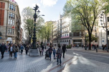Bilbao, İspanya, 4 Nisan 2024: Yayalar, dekoratif sokak lambaları, Kutxabank binası ve öğleden sonra aydınlığında bahar ağaçları ile Bilbao 'daki Gran Via, editoryal görüntü