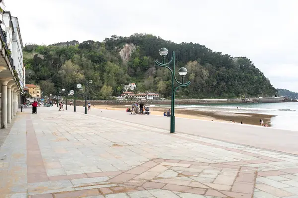 Zarautz, İspanya, 4 Nisan 2024: İspanya 'nın Zarautz kentinde sahil kenarında sahil kenarında yürüyen insanlar ve orman kayalıkları. Okyanus manzaralı bir kıyı yolu, editoryal görüntü