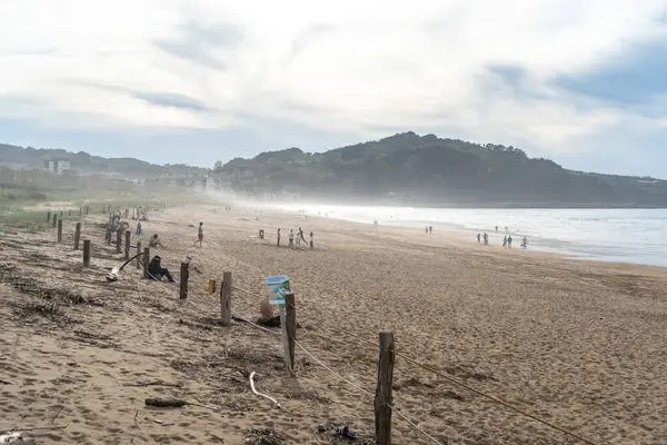 Zarautz, İspanya, 4 Nisan 2024: Zarautz plajı, arka planda çitlerle çevrili kumullar ve puslu tepeler, insanların deniz kenarında yürümeyi ve rahatlamayı sevdiği yer, editoryal görüntü