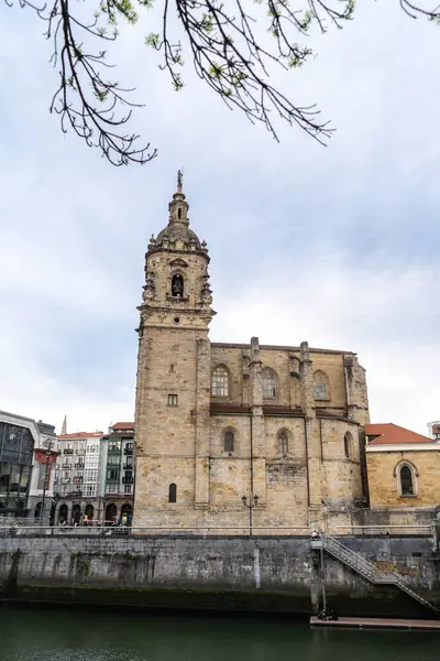 Bilbao, İspanya, 4 Nisan 2024: Eski Bilbao kasabasındaki Nervion Nehri boyunca çan kulesi ve nehir kenarındaki taş duvar ile Gotik tarzda San Anton Kilisesi, editoryal görüntü