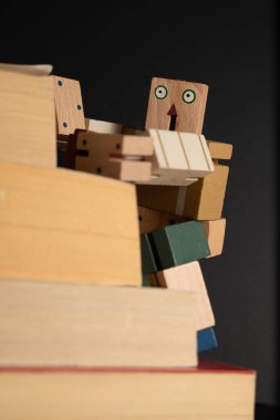 Tahta robot kitap yığınına tırmanıyor, okuma yoluyla öğrenme ve kişisel gelişim yolculuğunu temsil ediyor.