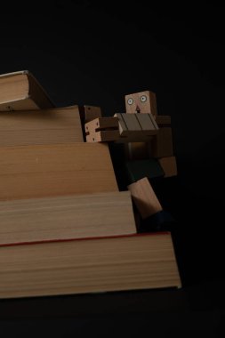 Tahta oyuncak sürekli öğrenme ve okuma yoluyla kişisel gelişim kavramını temsil eden kitap yığınına tırmanıyor.