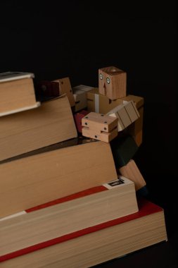 Tahta robot kitap yığınına tırmanıyor, okuma yoluyla bilgi ve kişisel gelişimi sembolize ediyor.