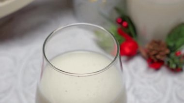 Birisi arka planda noel süslemeleri olan bir bardağa tarçın tozu serpiyor.