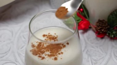 Geleneksel bir noel içeceği olan kremalı bir bardağa bir kaşık tarçın tozu ekliyorum.