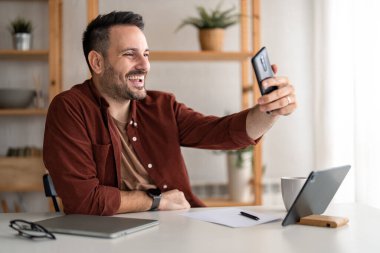 Gülümseyen yakışıklı milenyum adamı evde oturup işe ara verirken kendi portresini çekmek için akıllı telefon kullanıyor..