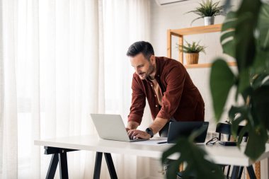 Memnuniyet duyulan yakışıklı milenyum adamı, ofis masasında otururken dizüstü bilgisayarda yazarken, e-postaya cevap verirken ya da internette ya da yerel belge klasöründe hızlı bir arama yaparken. Modern erkeklik kavramı.