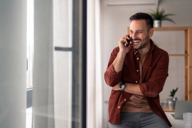 Güzel görünümlü, modaya uygun, günlük kıyafetler giyen ve cep telefonuyla konuşan, olumlu konuşan bir adam. Modern yaşam tarzı, bağlantı, iş konsepti.
