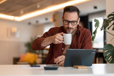Tablet kullanan ve kahve içen modern bir adam. Tablet üzerinde çalışan ya da kahve içerken haber okuyan bir erkeğin fotoğrafı..