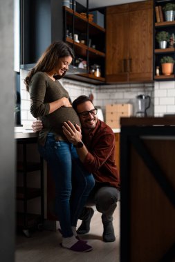 Şefkatli koca, sevgi dolu hamile karısının karnına dokunuyor, hayal kuruyor, bebeğin kalp atışlarını dinliyor, hamileliği boyunca ona destek oluyor..