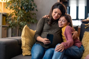 Değer veren bir kadın, bekar bir anne genç kızıyla birlikte oturma odasında kanepede otururken internetten e-kitap okuyor ya da çizgi film seyrediyor..