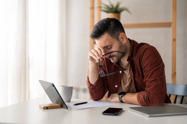Уставший сонливый бизнесмен, предприниматель, страдающий от психического выгорания, головной боли, снятия очков, испытывающий недостаток сна при работе над новым стратегическим планом проекта. Концепция домашнего офиса.