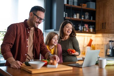 Yakışıklı adam ve sevgili eşi ve kızı birlikte yemek hazırlamak üzereler, bir dizüstü bilgisayardan online tarif arıyorlar..