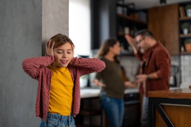 Anne ve babasının tartışmasını dinlememek için kulaklarını tıkayan üzgün küçük kız. Ailesinin kavgası yüzünden acı çeken üzgün görünümlü bir kız..