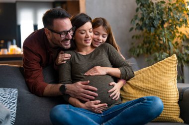 Sevgi dolu bir koca ve kız anne arkadan sarılıyor, karnına dokunuyor, kanepede dinlenirken sevgisini gösteriyor..