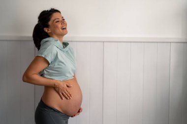 Güzel bir gülümsemesi olan, karnına el ele tutuşan, hamileliğinin son üç ayının tadını çıkaran çekici hamile bir kadın..