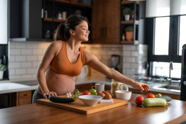 Müstakbel anne mutfakta taze organik sebzelerle salata hazırlıyor. Gülümsüyor. Sebzelere uzanırken.