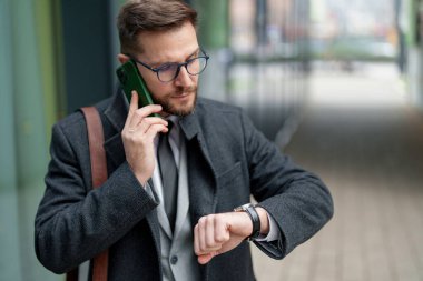 Akıllı giyimli orta yaşlı bir işadamı, bir gezici sohbete girişir, aynı zamanda kol saatine bakarak dakikliği sağlama alır, şehir arka planına karşı kurulur..