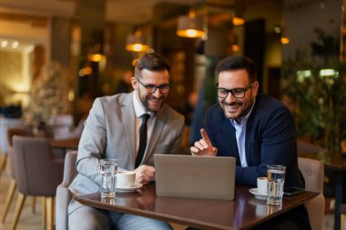 Takım elbiseli iki gülümseyen orta yaşlı adam, çağdaş bir kafe 'nin karşılama ortamında dizüstü bilgisayar kullanarak iş tartışmasına giriştiler..