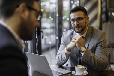 İş kıyafeti giymiş iki orta yaşlı beyaz adam bir kafede dizüstü bilgisayarla tartışıyorlar, kahve fincanları da sıradan bir buluşma ortamı öneriyor..