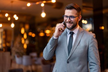 Genç işadamı telefonda konuşuyor. İş ortaklarıyla iletişim kurarken gülümseyen genç bir işadamı. Modern bir çalışma alanında başarılı bir girişimci.