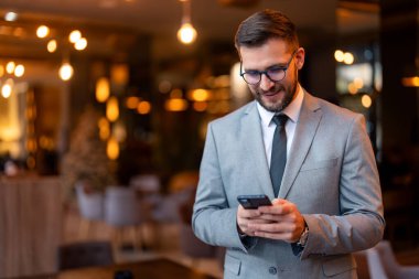 İş yerinde akıllı telefon kullanan genç bir iş adamı. Modern iş adamı müşterilerine mesaj gönderiyor. Modern bir iş yerinde tek başına duran iyi giyimli bir iş adamı..