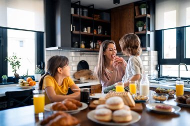 Küçük bir çocuk paylaşmayı seviyor, annesini çörekle besliyor. Çocuklar anneleriyle kahvaltı yapıyor..