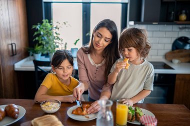 Anne çocuklarıyla birlikte evde mutfak masasında kahvaltı ederken..