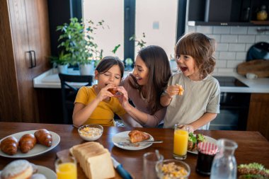 Çocuklar anneleriyle kahvaltıda kruvasan yiyorlar..