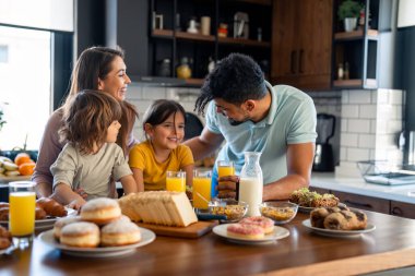 Küçük sevimli çocuk ve kız sabah anne ve babasıyla birlikte evde zengin lezzetli bir kahvaltı yapıyorlar..