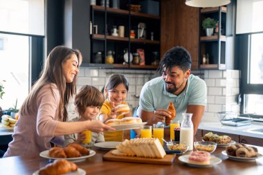 Mutlu ebeveynler çocuklarla kahvaltı yapıyor, küçük sevimli oğlan ve kız mutfakta..