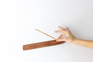 Tütsü çubukları için uzun kahverengi bir standın beyaz arka planında bir kadının eli geleneksel bir sete yeni bir bej meditasyon çubuğu koyar.