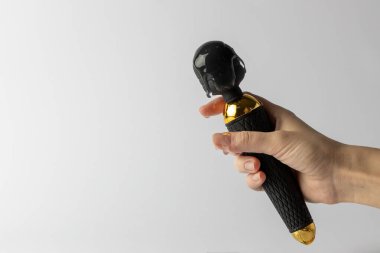 Parmaklarında kayganlaştırıcı olan beyaz arka plandaki kadının elinde, şeffaf su kayganlaştırıcı ve yetişkinler için cinsel zevk oyuncakları olan mikrofon şeklinde siyah bir vibratör var.