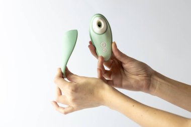 Beyaz bir arka planda kadın elleri süpürge vibratörü ve onun kapağı kızlar için hafifçe nane rengi renk cihazı yetişkinler için yumurta şekli manyetik su direnci şarj ediyor.