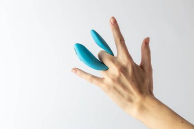 Beyaz arka planda, kadın parmaklarında mavi vibratör. Çifte giriş zevki için. İki su geçirmez modern cihaz için.