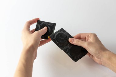 Beyaz arka plandaki bir kadının ellerine yakın plan. Siyah pakette üç prezervatiften birini aç. Güvenli seks korunması.