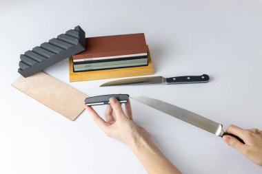 white background on counter lies all the equipment - a set for sharpening and polishing kitchen knives - the girl's hands are fixing the fuse and the locking device for knife protection against cuts clipart