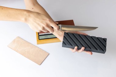 Tezgahın üzerindeki beyaz arka planda mutfak bıçaklarını bilemek ve cilalamak için tüm set uzanıyor. Kızın elleri ön planda siyah bir taş ve bir bıçak tutuyor.