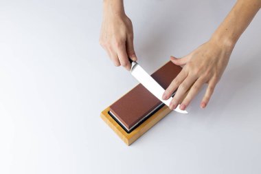 on a white background on a table, women's hands sharpen a steel knife, a lock under the arm, protection against cuts, a red medium-hard stone for sharpening knives clipart