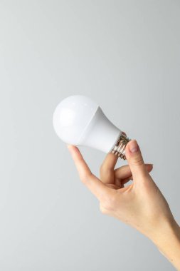 Yan taraftaki beyaz arka planda, bir kadının ince eli geniş tabanlı, ekonomik enerji tüketimi, nötr renk, aydınlatma elementi olan beyaz bir ampulü tutar.