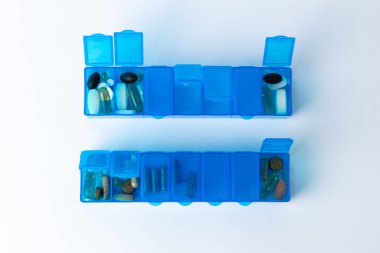 Üst çekimde beyaz arka planda haplar, sağlık hizmetleri, kısmi dolgu, farklı şekiller, haplar ve vitaminlerin renkleri ve renkleri için açık kapaklı iki adet parlak mavi hap kutusu var.