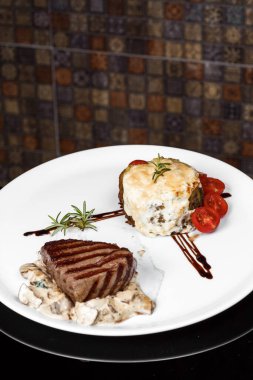 Üst düzey profesyonel mutfak beyaz tabak dana madalyonu mantar yatağında balzamik soslu karaciğer ezmesi ve taze vişneli domates restoranı biberiye filizi servis ediyor.