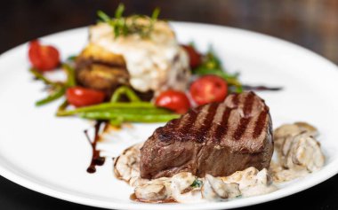 Üst düzey profesyonel mutfak beyaz tabak dana madalyonları balzamik soslu mantar soslu karaciğer ezmesi ve taze vişneli domates lokantasında biberiye filizleri servis ediliyor.