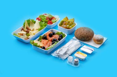 Havayolları için mavi arka plan yemeği tek kullanımlık sofra takımı dilimlenmiş peynir fındıklı taze sebzeler ve zeytinli somon somonu krem peynirli çörek ezmesi ve tek kullanımlık sofra takımı.